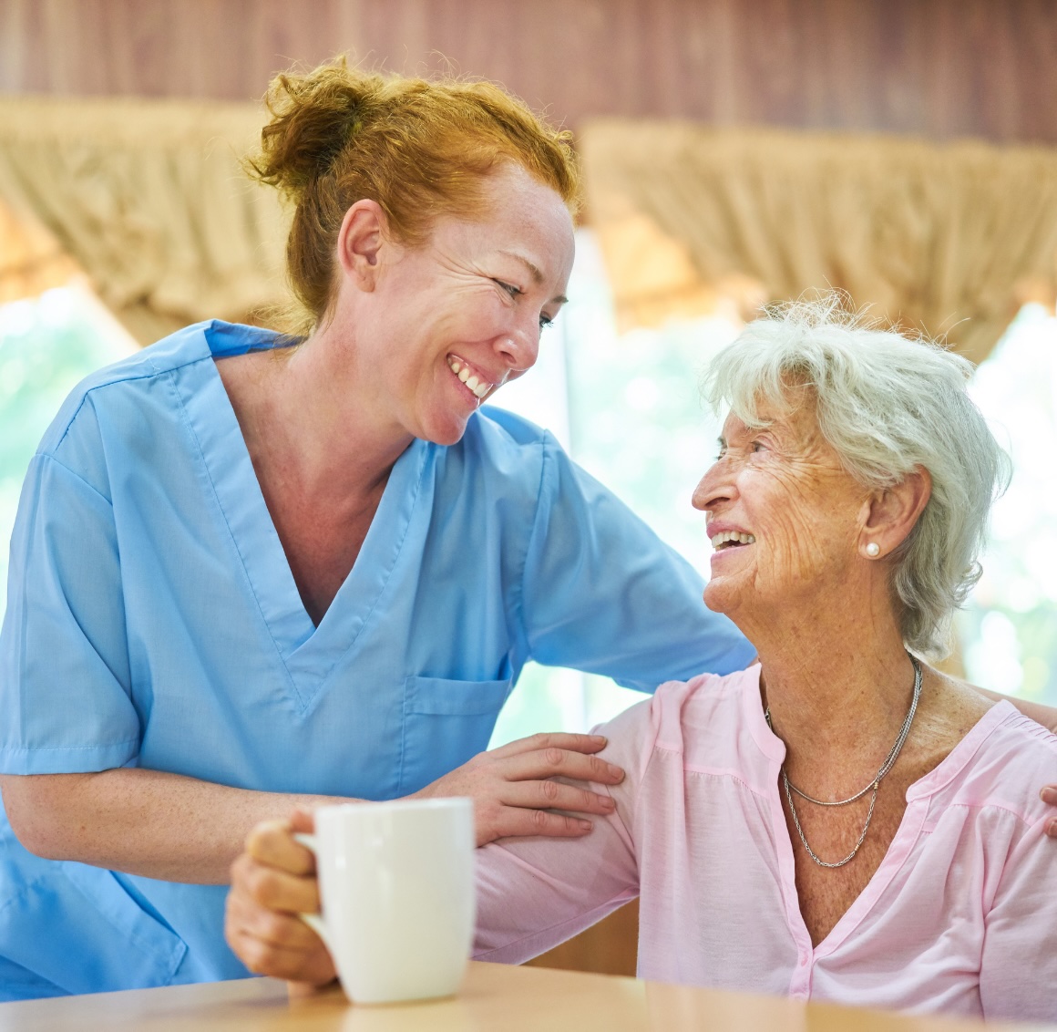 A caregiver holds and helps a older client at home, representing the type of quality caregivers that can help with light housekeeping in Reno.