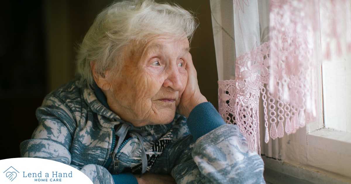 An older woman peacefully looks out of the window while the sun is still up, representing what can happen with sundowning.
